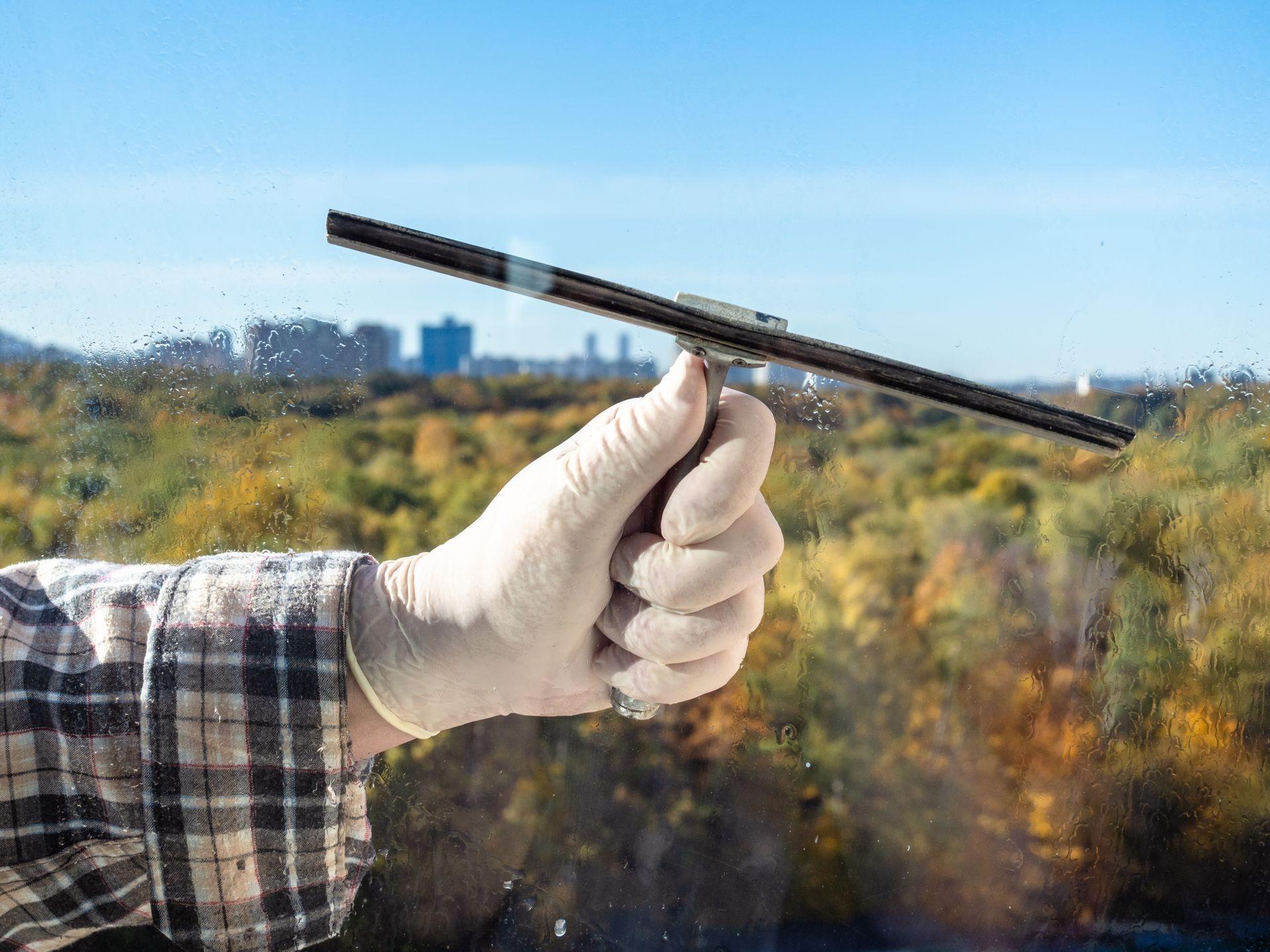 male hand washes a home window glass by squeegee in sunny autumn day